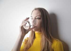 girl wearing a yellow turtle neck drinking a glass of water, a lifestyle for healthy brain