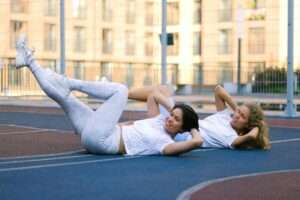 two young ladies doing bicycle crunches exercises outdoors 