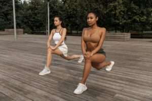 two young women doing lunges fitness exercise outdoors