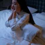 The main causes of insomnia, a woman in white long sleeve shirt sitting on a bed having insomnia